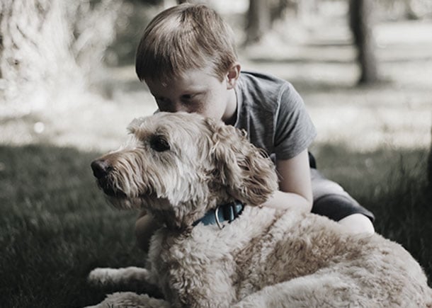 A boy cuddling with a dog in the grass